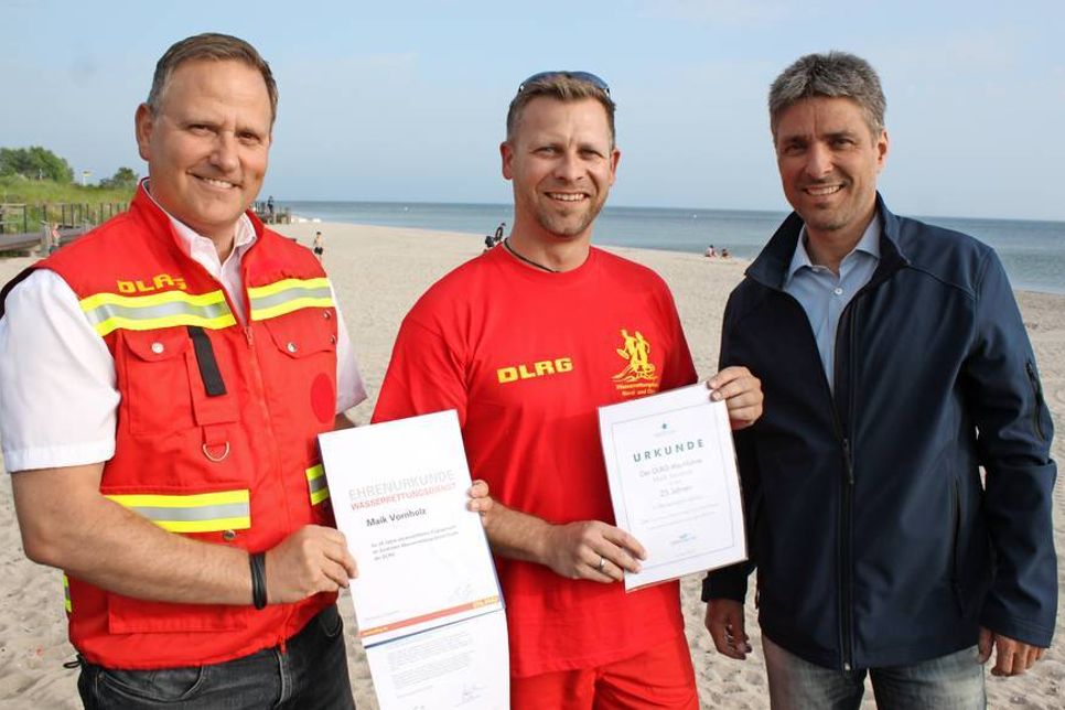 Maik Vornholz (Mitte) leistet seit 25 Jahren Wachdienst in Pelzerhaken. Es gratulierten Stephan Reil vom Tourismus-Service Neustadt-Pelzerhaken-Rettin (re.) sowie Klaus Holger Hecken.