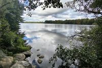 Michael Tholen zeigt den Kleinen Eutiner See von seiner stillen Seite – mit spiegelglattem Wasser und bewegtem Himmel.