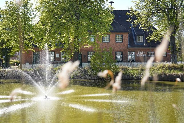 Idyllischer Blick auf Schönwalde: Im Vordergrund der Mühlenteich mit Wasserspiel, dahinter das Dorf- und Schulmuseum in der ehemaligen Dorfschule.