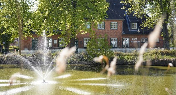 Idyllischer Blick auf Schönwalde: Im Vordergrund der Mühlenteich mit Wasserspiel, dahinter das Dorf- und Schulmuseum in der ehemaligen Dorfschule.