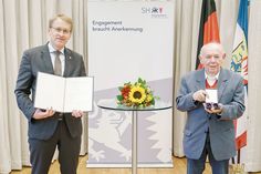Aus den Händen von Ministerpräsident Daniel Günther nimmt Jurek Szarf für seine Erinnerungsarbeit das Bundesverdienstkreuz entgegen.