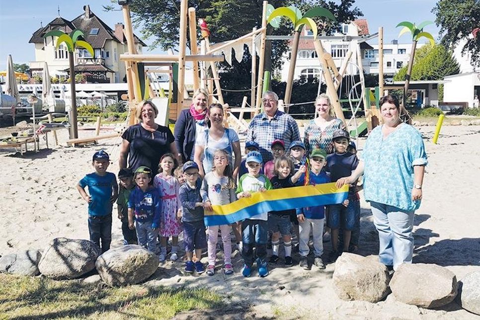 Gruppenfoto kurz vor dem Durchschneiden des Bandes: Bürgervorsteherin Anja Evers, der 2. stv. Bürgermeister Andreas Müller und Gesine Muus, Werkleiterin des Kurbetriebes, mit Erzieherinnen und Kindern des Evangelischen Kindergartens Timmendorfer Strand.