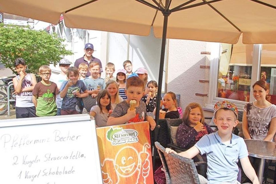 Sommergefühle in der Eisdiele Bertow. Eine ganze Schulklasse genießt das wunderbare Eis, zu dem Eigentümer René Bertow (hinten mit Schirmmütze) sie eingeladen hat. Lehrerin Katharina Kiefel (rechts) freut sich über das gelungene Experiment.