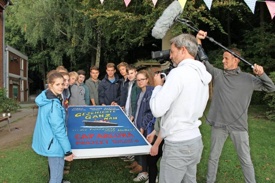 Geschichte ganz nah: Die Schüler präsentierten das Plakat zum Projekt für das begleitende Kamerateam mit SKY-Moderator Jens Westen (re.) am Umwelthaus.