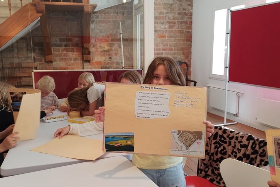 Schülerinnen und Schüler der Grundschule Neustädter Bucht präsentieren selbst gestaltete Plakate mit Bildern und kurzen Texten über Neustadt.