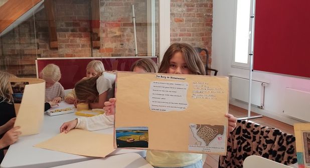 Schülerinnen und Schüler der Grundschule Neustädter Bucht präsentieren selbst gestaltete Plakate mit Bildern und kurzen Texten über Neustadt.