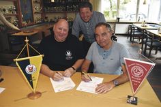 Die Vorsitzenden der beiden Vereine, Jörg Henkel (TSV Neustadt, links) und Andreas Block (NTSV Strand 08), unterschreiben den Genehmigungsantrag zur Bildung einer Spielgemeinschaft, der jetzt beim Schleswig-Holsteinischen Fußballverband eingereicht wurde. Fußballabteilungsleiter Max Thole (NTSV) schaut Beiden über die Schulter. (Foto: René Kleinschmidt)