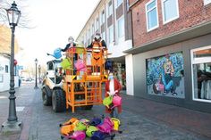 Sabine Bockwoldt, auf dem Hubwagen mit Philip Möller von den Kommunalen Diensten Oldenburg, und Cora Brockmann legen beim Aufhängen der Gießkannen Hand an.