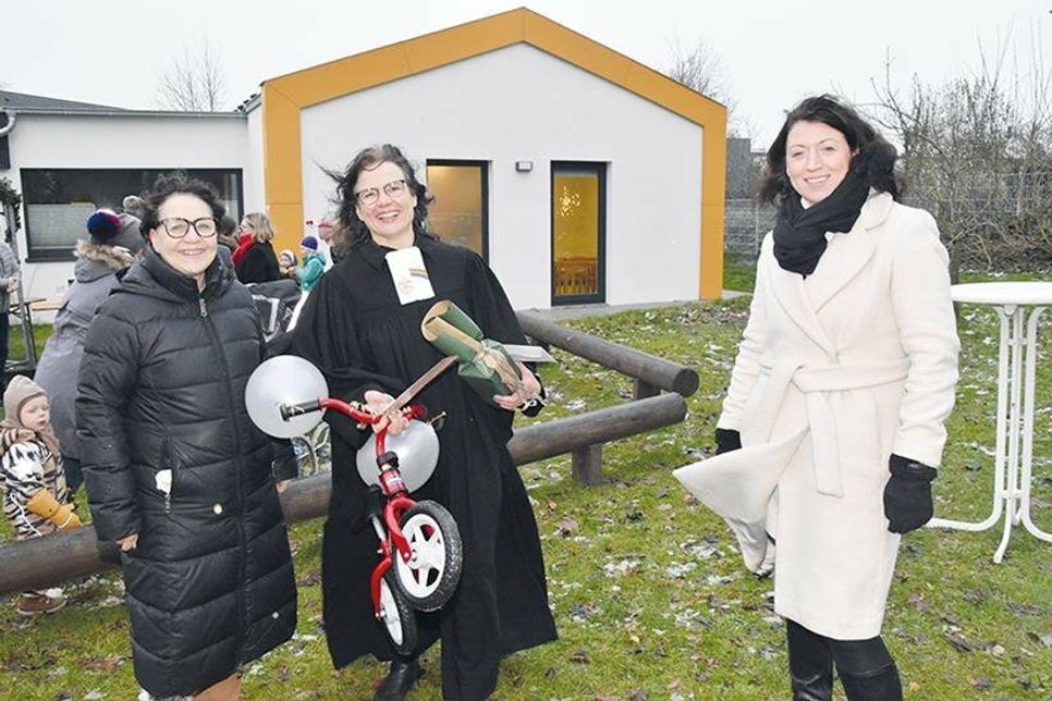 Kita-Leiterin Gudrun Ovens (links), Pastorin Corinna Schlapkohl (mit Geschenken zur Einweihung) und Bürgermeisterin Bettina Schäfer vor dem Erweiterungsbau der Kita in der Schmiedestraße.