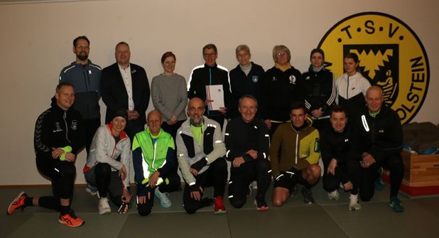 Mit dem frischgebackenen „Moin! Vereinsheld des Monats Januar“ Peter Massny (stehend Mitte, mit Urkunde) freuen sich Wiebke Watzlawek (Stiftungen der Sparkasse Holstein), Fabian Wierichs (Sparkasse Holstein, beide links vom Geehrten), Birgit Kamrath-Beyer (KSV Ostholstein) und Anett Virsnitis (TSV Neustadt, beide rechts vom Geehrten) sowie das Laufteam des TSV Neustadt. (Foto: Carsten Stender, Kreissportverband Ostholstein)