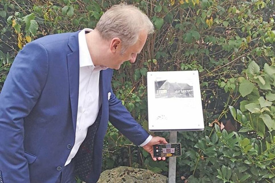 Bürgermeister Peter Kokocinski scannt den QR-Code, durch den die Informationen digital verfügbar werden.
