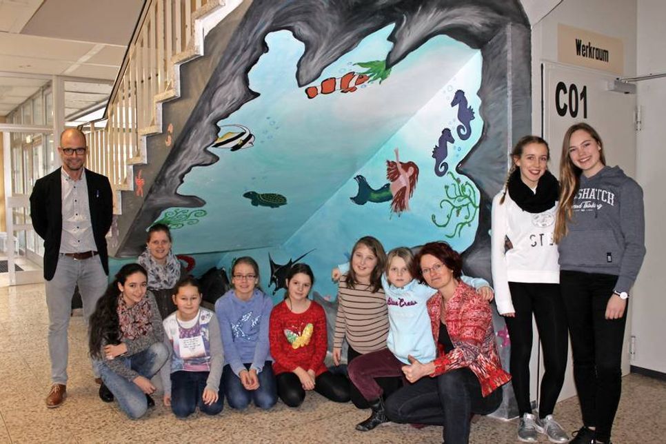 Schulleiter Karsten Kilian (lks.), Birte Anika Schröder (hi.) und Anne Kraatz (vorne re.) vor der „Unterwassergrotte“ unter der Treppe.