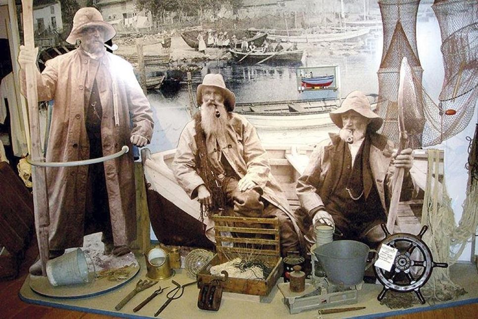 Das Wandbild im Hintergrund zeigt den Travemünder Fischereihafen um 1908, davor ist eine Fischergruppe (um 1900) zu sehen. (Foto: Seebadmuseum)
