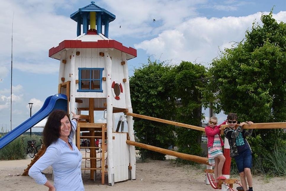 Bettina Schäfer, Leiterin des Bauhofs in Scharbeutz, präsentiert den neuen „Leuchtturm-Spielplatz“, der von den Geschwistern Constantin und Henriette, die in Scharbeutz Urlaub machen, direkt getestet wird.  (Foto: Eknad)