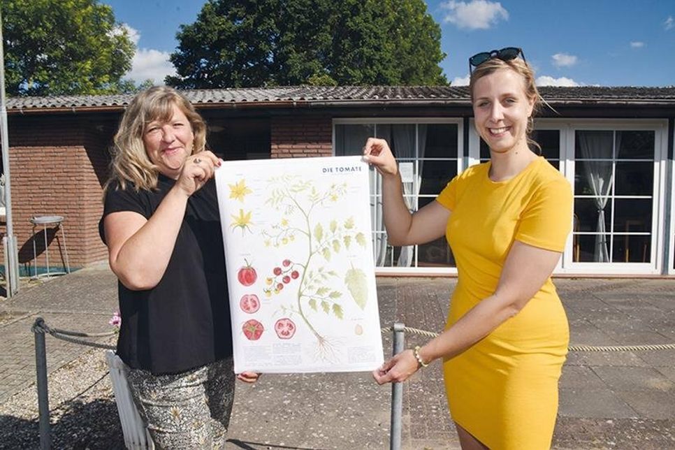 Kassenwartin Martina Böckmann (links) und Anna Karamnow zeigen ein Plakat über den Aufbau der Tomate, das Anna mit ihrer Schwester Emma gestaltet hat.