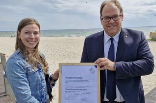 Bürgermeister Mirko Spieckermann und Nachhaltigkeitsmanagerin Lina Sophie Koop mit der Auszeichnung für die erfolgreiche Projektteilnahme „BNK bundesweit 2024“, in dessen Rahmen die Berichtserstellung nach dem Berichtsnahmen Nachhaltige Kommune (BNK) erfolgte. (Foto: Stadt Neustadt in Holstein)