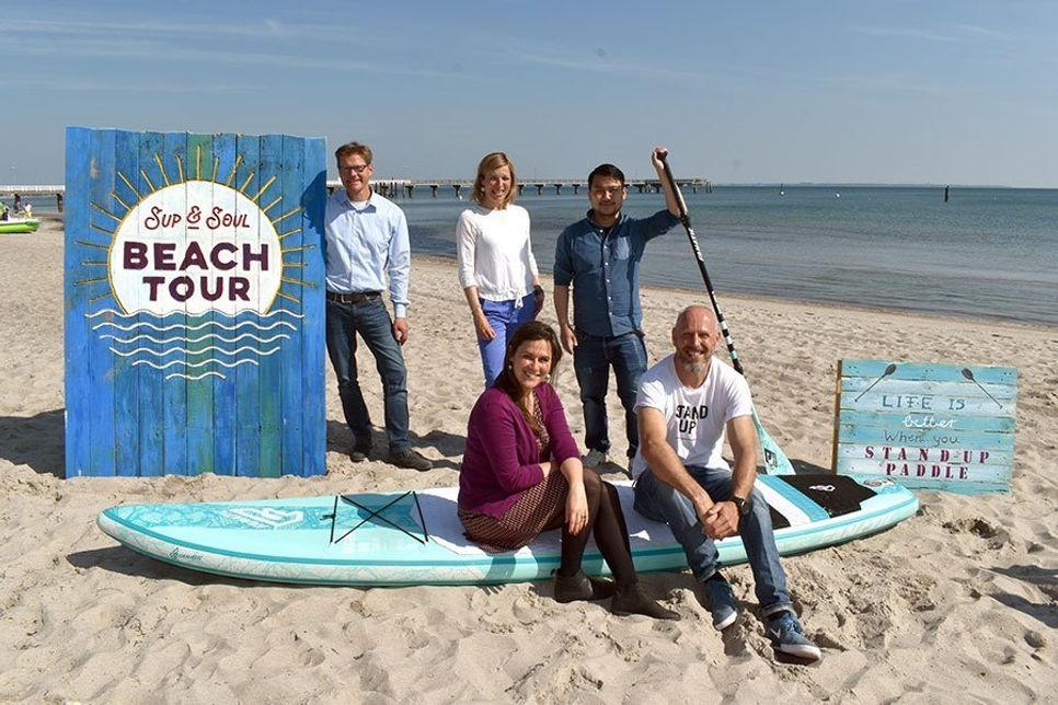 Joachim Nitz (Geschäftsführer TSNT GmbH, hinten von links), Christine Knebelkamp (Veranstaltungsabteilung TSNT GmbH), Thuan Nguyen ( Tourismus-Service Grömitz) und Tabea Braun (Tourismus-Agentur Lübecker Bucht, vorne links) freuen sich mit Dirk Herpel (Organisator) auf die SUP &amp;amp; SOUL Beach Tour in der Lübecker Bucht, die in Timmendorfer Strand startet. (Foto: René Kleinschmidt)