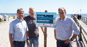 Links von der Seebrücke soll in Zukunft auf einem Abschnitt von circa 150 Metern nicht mehr geraucht werden, auf freiwilliger Basis. Stephan Reil vom Tourismus-Service, Ortsbeiratsvorsitzender Lars Prigge und Bürgermeister Mirko Spieckermann (v. lks.) präsentierten die neu aufgestellten Schilder.