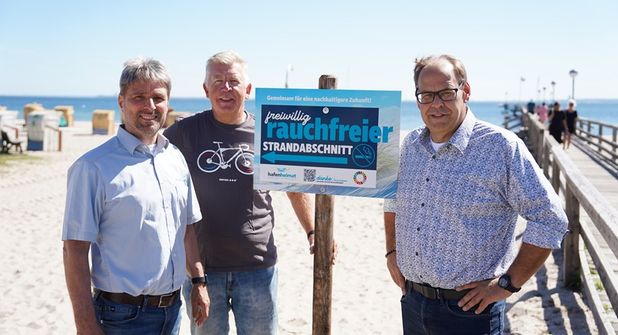 Links von der Seebrücke soll in Zukunft auf einem Abschnitt von circa 150 Metern nicht mehr geraucht werden, auf freiwilliger Basis. Stephan Reil vom Tourismus-Service, Ortsbeiratsvorsitzender Lars Prigge und Bürgermeister Mirko Spieckermann (v. lks.) präsentierten die neu aufgestellten Schilder.