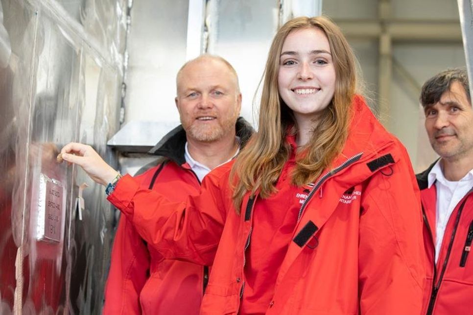 Unter den Augen ihres Vaters und Seenotretter Markus Davids (l.) sowie Vormann Guido Förster hält Merle Davids die Bremer Zwei-Euro-Münze für die Fotografen schon einmal an die richtige Stelle, bevor sie sie endgültig in die Aluminiumtasche fallen lässt.
