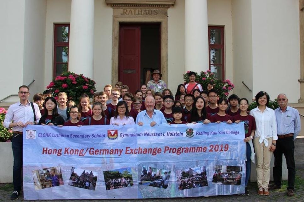 Die beteiligten Schüler und Lehrer aus Hong Kong und Neustadt posieren mit Bürgervorsteher Sönke Sela (Mi.) vorm Rathaus.