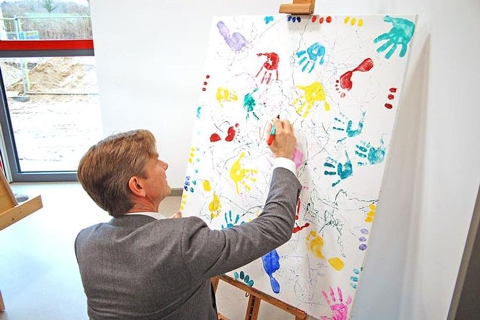 Sozialminister Heiner Garg signiert ein Bild, das die Kinder für ihn und andere Ehrengäste gemalt haben.