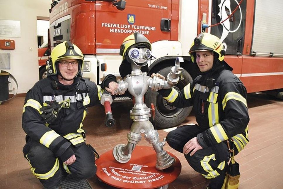Gruppenführer Jens Krüger (rechts) hat den „Feuerwehrmann der Zukunft“ aus ausgemusterten Feuerwehr-Armaturen gebaut. Mirco Babin von der Jugendfeuerwehr freut sich mit ihm über „Nieno“, der um neue Kameraden wirbt.