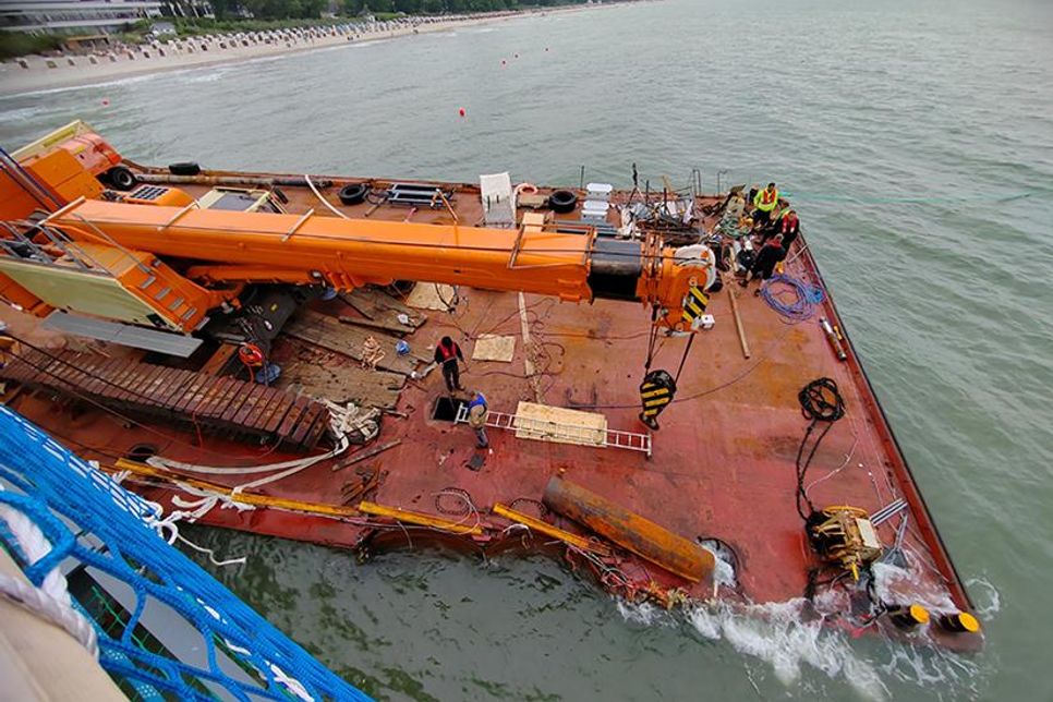 Blick von der neuen Seebrücke auf den gestrandeten Arbeitsponton, in dem Taucher versuchen, die beschädigten Kammern zu reparieren und leer zu pumpen. Zum Einstieg mit Taucherausrüstung musste extra das Deck großflächig per Schweißbrenner aufgeschnitten werden.