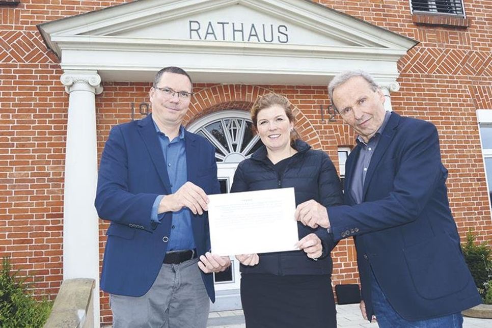 Jens Clauß (r.) und Patrick Lakins aus dem Vorstand des Gemeinnützigen Bürgervereins Stockelsdorf übergeben eine Kopie der Urkunde an Stockelsdorfs Bürgermeisterin Julia Samtleben.