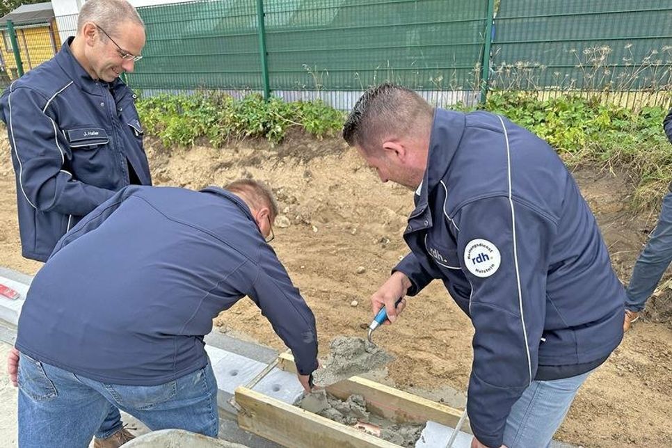 Beim Einbetonieren der mittlerweile durch einen Handwerker verlöteten und als Zeitkapsel dienenden Blechhülse im Fundament, von rechts nach links: Christian Kraft (Vorstand rdh.), Claus Hopp (Wachleiter Rettungswache Oldenburg), Jörn Haller (Teamleiter Facility der rdh.)
