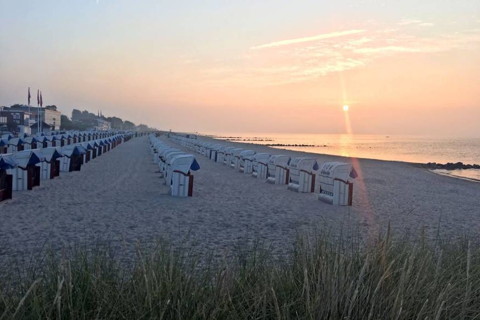 Grömitz: Das macht Lust auf viel Meer. Seebrückenvorplatz, Strandkörbe und der Himmel von der Morgenröte verfärbt.
