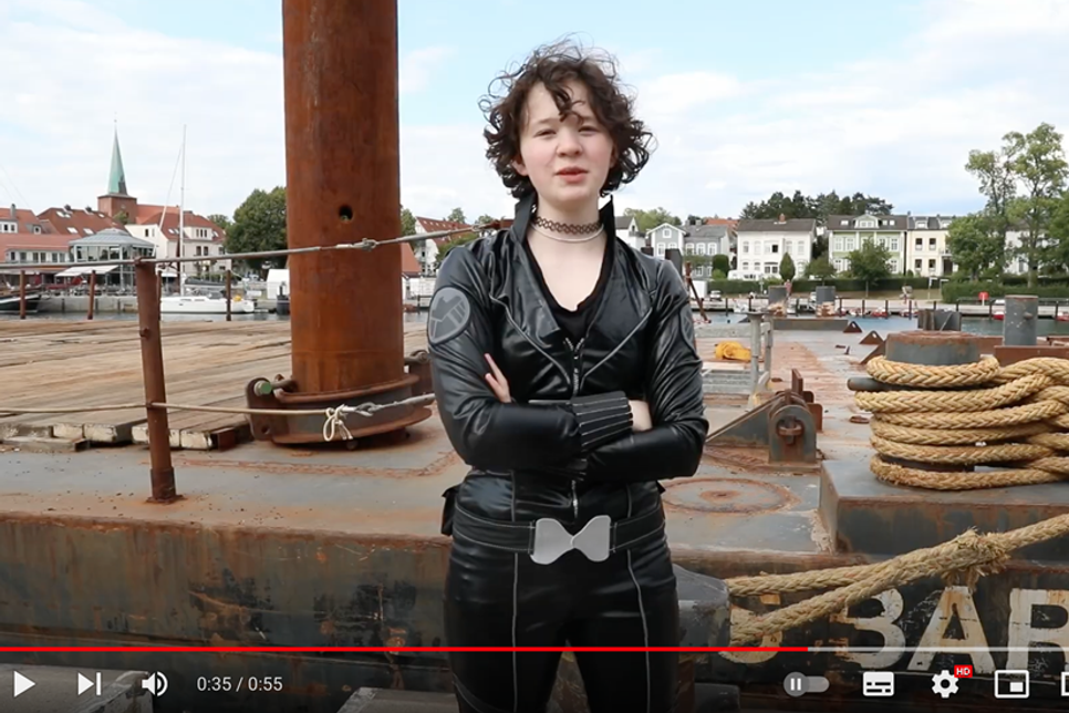 Screenshot von einer Black-Widow-Szene: Kijupa-Mitglied Finja als „Black Widow“ vor der Kulisse des Neustädter Hafens.