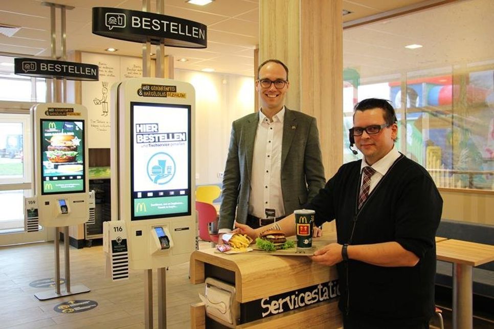 Kevin Neubaumer (lks.) und Mitarbeiter Dirk Fiedler präsentieren die neuen Bestellsäulen und ein Menü der neuen Gourmetlinie, die auf schmucken Holzbrettern serviert wird.