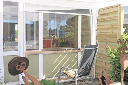 Fensterkontakt: Geschützt vor Regen und Sonne sitzen Besucher draußen und Bewohner im Wintergarten hinter der Scheibe.