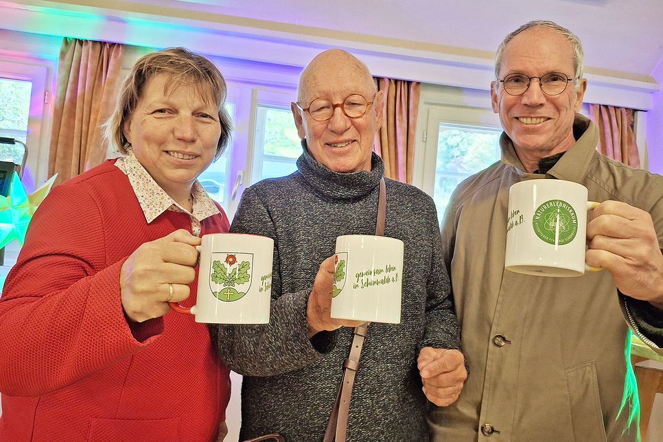 Die stellvertretende Bürgermeisterin Angela Hüttmann sowie Michael Schmidt und Arnd Heling vom Freundeskreis des Pfarrhofs Schönwalde präsentieren die neuen Tassen mit dem Slogan „Gemeinsam leben in Schönwalde“.