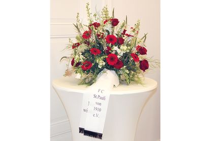 Der übergebene Blumenkranz mit dem Vereinsnamen und der schemenhaft zu erkennenden Inschrift „Nie wieder“.