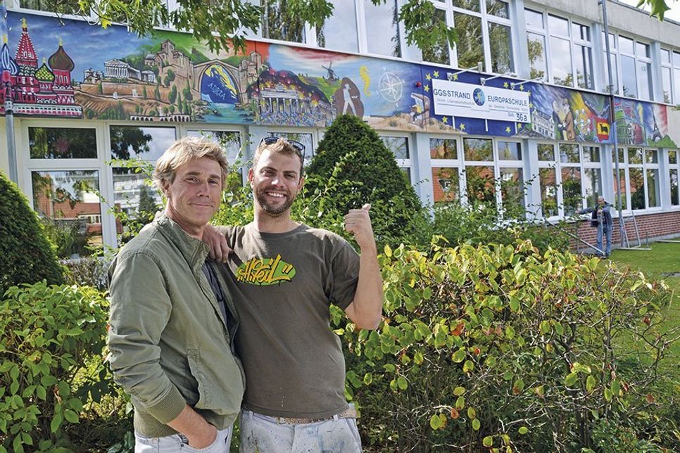 Ekkehard Rawohl, Klassenlehrer der 10 b, und Urban Artist und Street Art-Künstler Henning Marten Feil (re.) vor dem fertiggestellten Wandgemälde zum Thema „Europa“. (Foto: René Kleinschmidt)