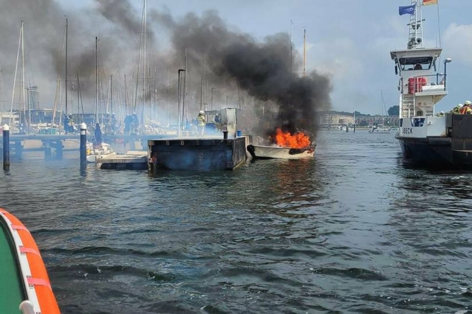 Das Seenotrettungsboot ERICH KOSCHUBS nähert sich dem brennenden Havaristen. Die Priwallfähre „Pötenitz“ bringt Feuerwehrleute von der Wasserseite aus zum Unglücksort.