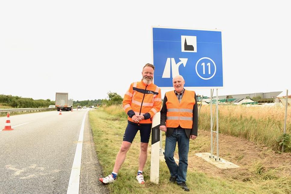 Verkehrs- und Tourismusminister Claus Ruhe Madsen und Hubertus Lürbke, pastoraler Leiter der Autobahnkirche an den frisch aufgestellten Schildern an der A1