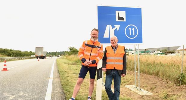 Verkehrs- und Tourismusminister Claus Ruhe Madsen und Hubertus Lürbke, pastoraler Leiter der Autobahnkirche an den frisch aufgestellten Schildern an der A1