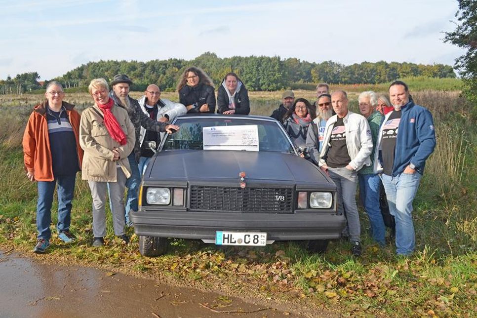 Beate Rinck und ein großer Kreis der US Classics Ostholstein trafen sich zur Geldübergabe an dem Platz, wo das Hospiz entstehen wird.