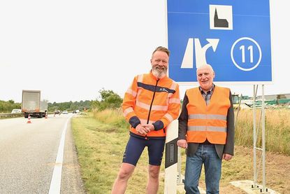 Verkehrs- und Tourismusminister Claus Ruhe Madsen und Hubertus Lürbke, pastoraler Leiter der Autobahnkirche an den frisch aufgestellten Schildern an der A1.
