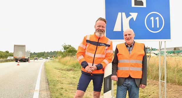 Verkehrs- und Tourismusminister Claus Ruhe Madsen und Hubertus Lürbke, pastoraler Leiter der Autobahnkirche an den frisch aufgestellten Schildern an der A1.