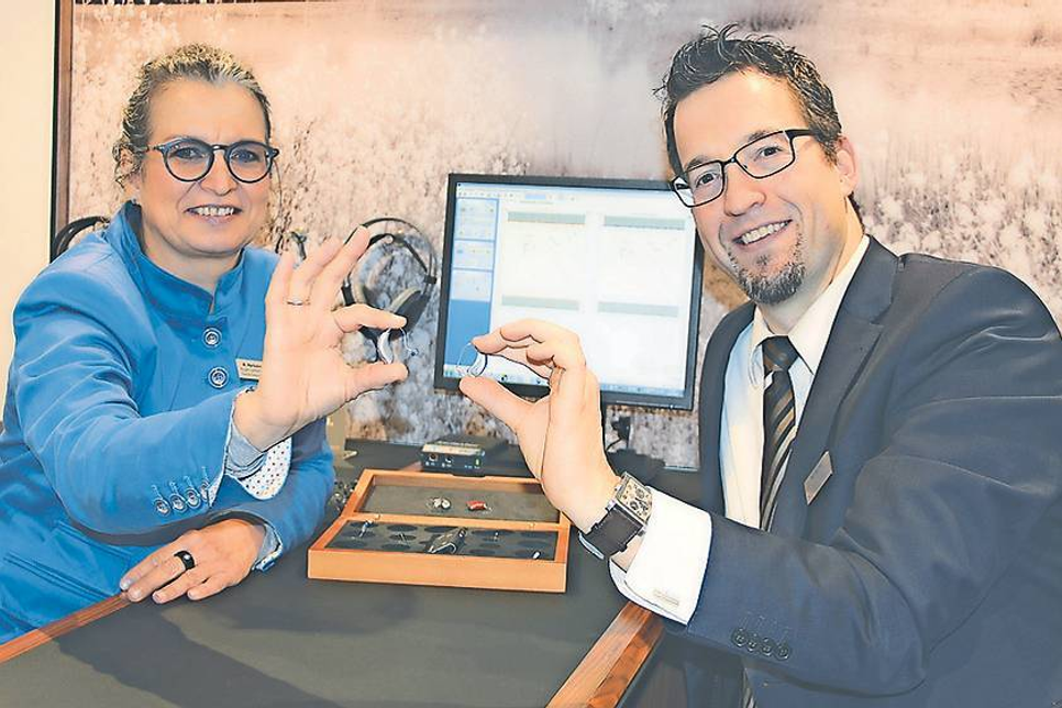 Hörgeräteakustikmeister Hermann Josef Assies und Niederlassungsleiterin Andrea Herkelmann zeigen Beispiele für moderne Hörsysteme, die in der Lage sind Störgeräusche wie Wind und Straßenlärm zu reduzieren und den Fokus der Geräuschaufnahme automatisch auf den Gesprächspartner zu lenken. Auch sind diese Geräte nicht nur von Hand, sondern auch per Fernsteuerung oder Handy-App bedienbar.