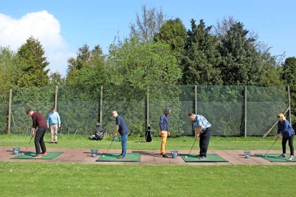 Abschläge auf der Driving Range unter den Blicken der Golflehrer.
