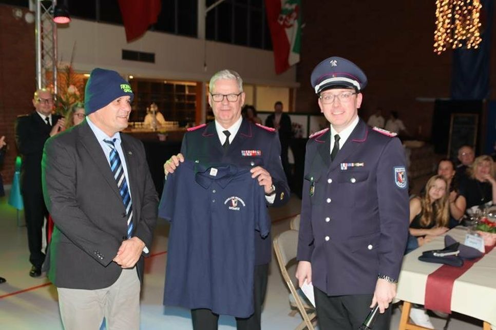 Mütze und T-Shirt für den Bürgermeister: Mark Burmeister wurde von Ortswehrführer Jacob Revenstorf und seinem Stellvertreter Kai Fischer (Mi.) ausgestattet.  (Foto: Christian Lück)