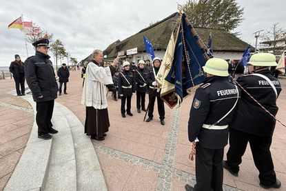 Pater Ralf Winterberg segnet auf dem Nystedplatz in Dahme die neue Fahne der Freiwilligen Feuerwehr.