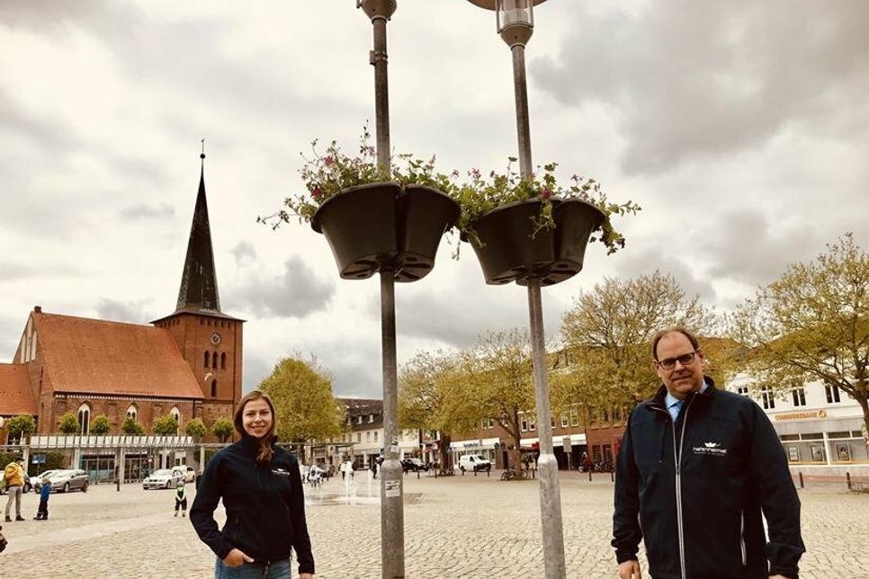 Bürgermeister Mirko Spieckermann und die Nachhaltigkeitsmanagerin Lina Koop vor den Blumenampeln am Marktplatz.