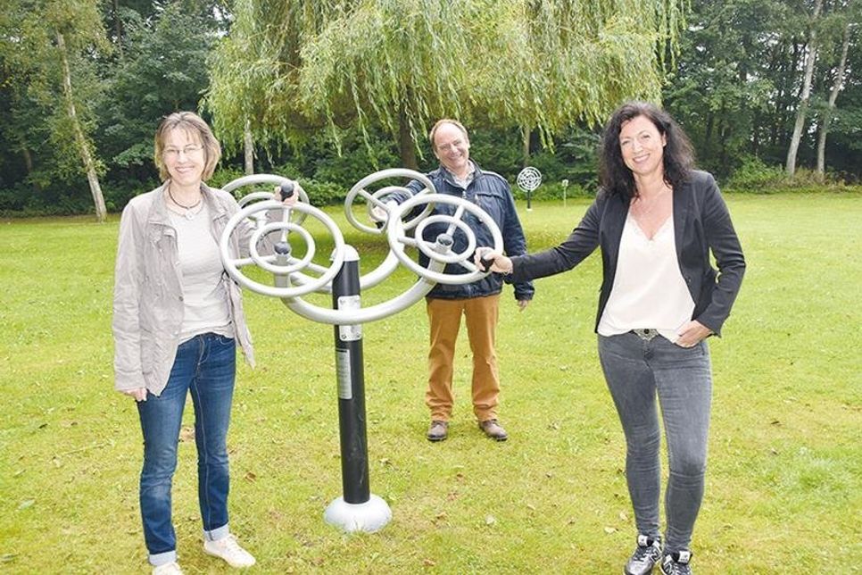 Tanja Schridde von der Aktiv-Region (von links), Dorfvorsteher Dierk Dürbrook und Bürgermeisterin Bettina Schäfer, die hier am „Steuerrad“ stehen, freuen sich über den neuen Fitness-Parcours im Paul-Zimmermann-Seepark in Klingberg.