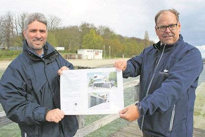 Bürgermeister Mirko Spieckermann (re.) und stellvertretender Werkleiter Stephan Reil zeigen die Pläne für die neue Wasserrettungsstation. Im Hintergrund das bestehende Gebäude.